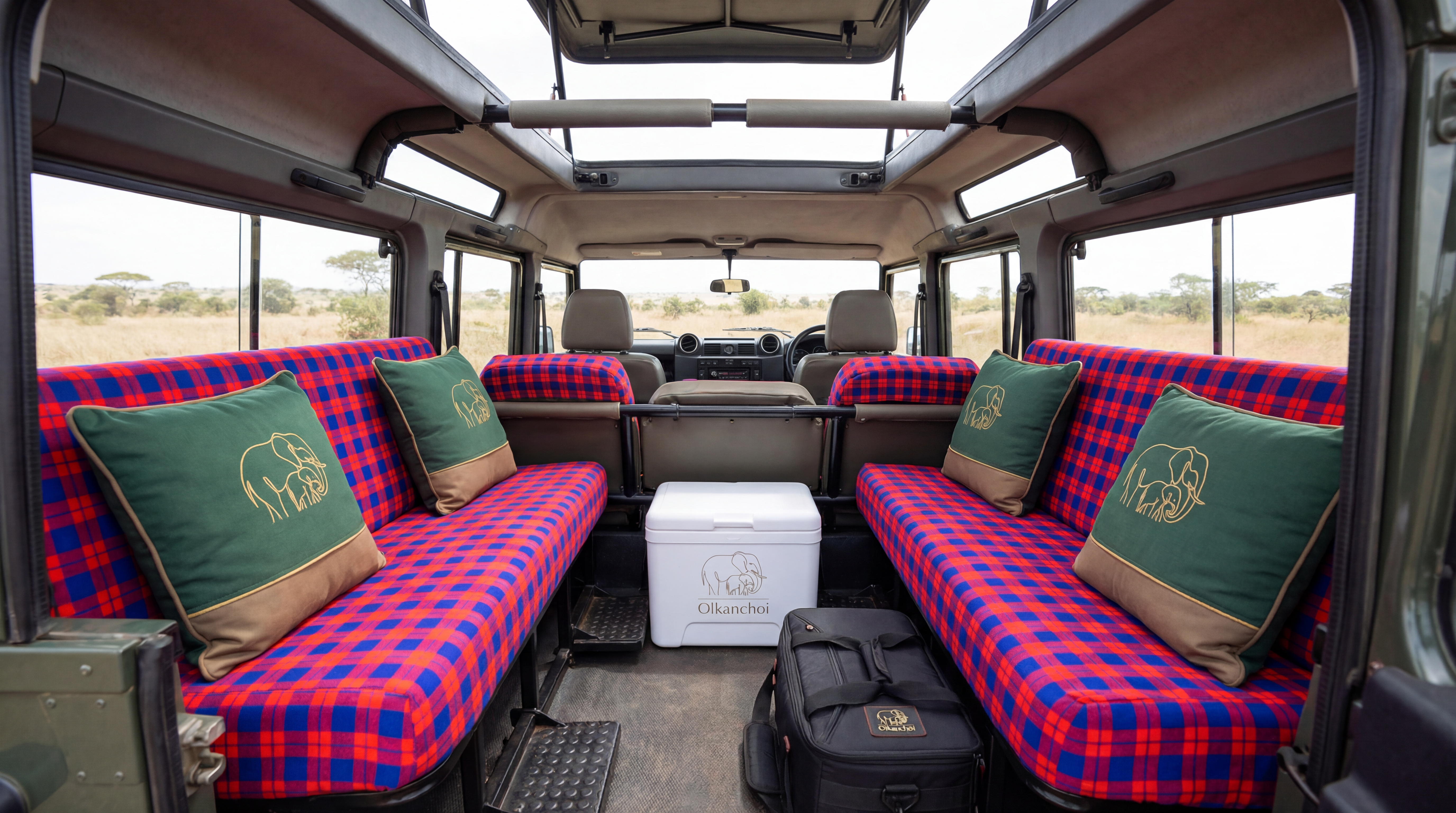 Interior of an Olkanchoi pop-top safari vehicle with Maasai-plaid seats and branded pillows overlooking the savanna