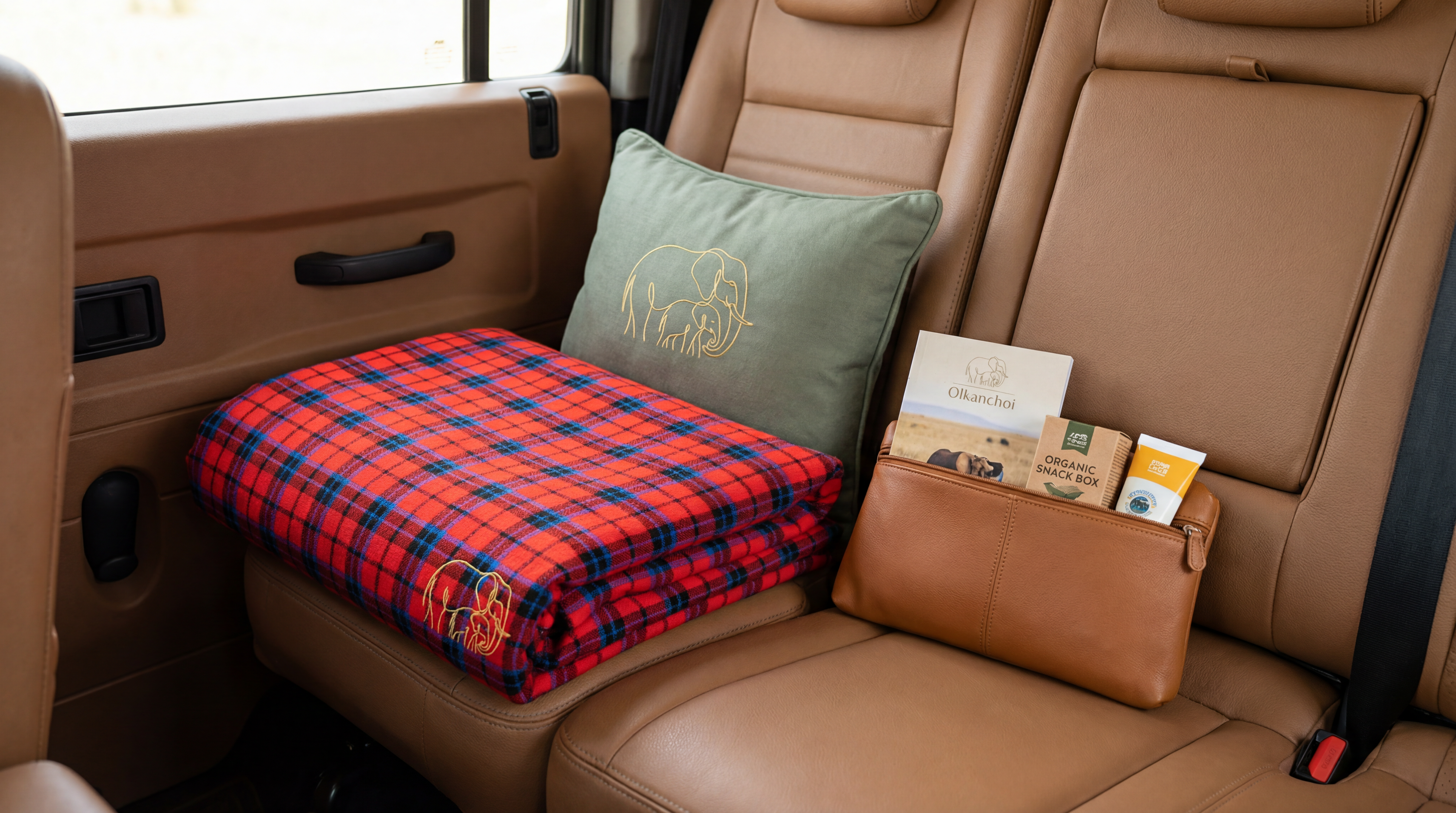 Olkanchoi welcome pack — folded plaid blanket, branded pillow and organic snack box on a leather seat